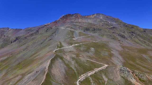 Winding Gravel Road Climbing a Mountainside in Mestia, Samegrelo Zemo Svaneti, Georgia, Under a Clear Blue Sky
