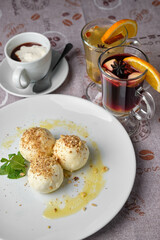 A delightful dessert, featuring round treats sprinkled with nuts, fresh mint, and a cup of coffee with whipped cream, all on a white plate.
