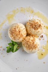 A delightful dessert, featuring round treats sprinkled with nuts, fresh mint, and a cup of coffee with whipped cream, all on a white plate.
