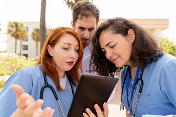 Medical professionals analyzing digital health records, collaborating outdoors near clinical setting during team consultation