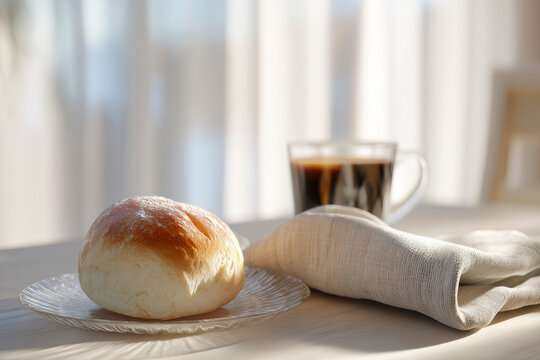Bright morning scene: Pastry roll on glass plate with dark drink, soft light, peaceful breakfast setting.