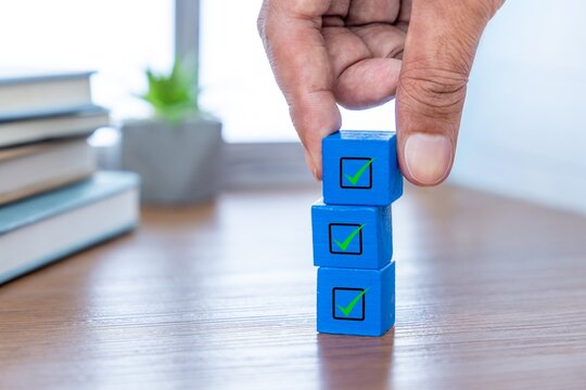 A hand stacking three wooden blocks with a green checkmark. Task completion, productivity, to-do lists concept.