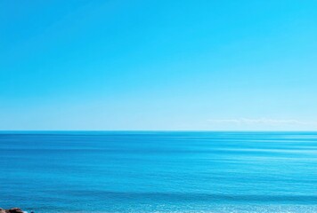 Obraz premium A serene seascape features tranquil azure waters meeting a clear, vibrant blue sky at the horizon. Gentle light reflects on the calm water's surface