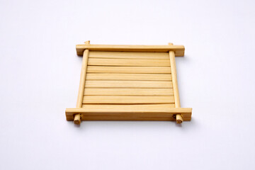 A minimalist, square-shaped bamboo coaster sits on a bright, white background. The clean, natural wood design features parallel slats held together by a simple frame.