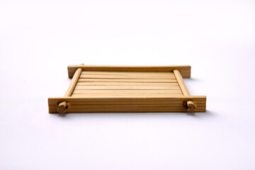 A minimalist, square-shaped bamboo coaster sits on a bright, white background. The clean, natural wood design features parallel slats held together by a simple frame.