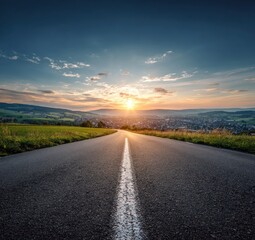 Scenic asphalt road stretching towards a vibrant sunset over a distant town, showcasing open skies and rural landscapes