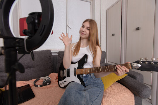 Young woman plays guitar while streaming a live session from her cozy living room - Powered by Adobe