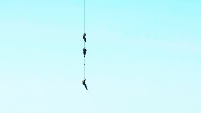 Three military paratroopers in the air against the sky descend into a landing rope. Demonstration performance. Copy space for text