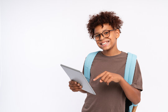 African-American school preteen boy elementary primary pupil in eyeglasses with backpack holding using digital tablet wireless electronic gadget promoting online app studio shot isolated copy space
