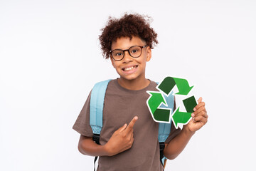 Curly African-American boy kid child elementary primary male pupil holding in hands pointing on recycling sign symbol isolated over white background copy space. Ecological sorting garbage concept