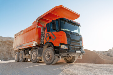 Large orange dumper truck working in a quarry transporting sand and gravel