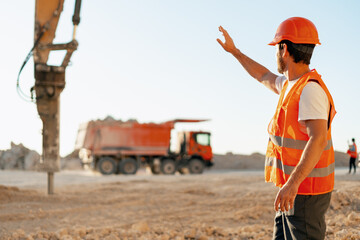 Construction worker directing excavator and truck on site