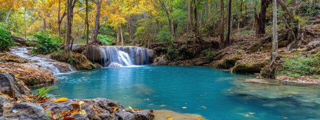 Vivid turquoise waters pool beneath gentle waterfalls amid an autumnal forest, trees displaying vibrant yellow and green foliage