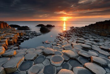 Hexagonal basalt columns meet the ocean under a dramatic sunset sky. Warm colors and textures create a captivating scene