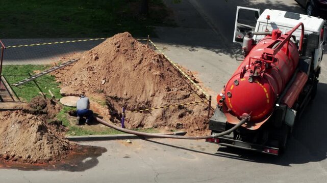 A male worker sucks out sewage from a manhole against the background of a truck with a tanker. Water supply and sewerage accident. Copy space for text, industry