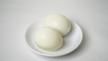 Peeled boiled eggs served on a white plate with a white background