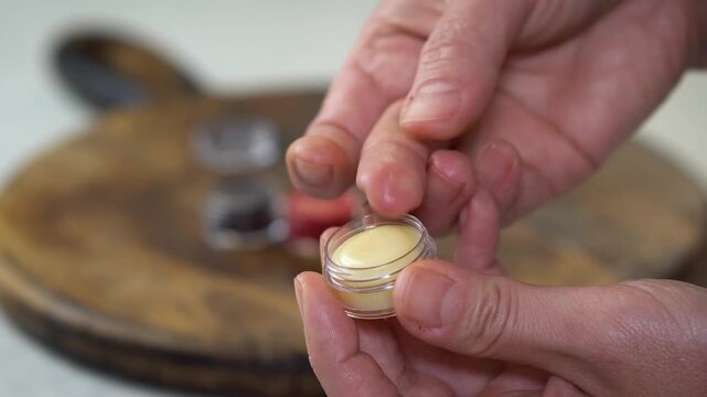 Checking the consistency of natural homemade lip balm in small transparent container. DIY organic skincare, eco-friendly beauty, artisanal cosmetics, and handcrafted sustainable style.