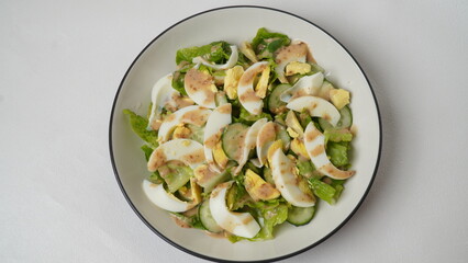 A serving of salad consisting of sliced ​​romaine lettuce, Japanese cucumber (kyuri), and boiled egg then topped with roasted sesame salad dressing served on a white plate and white background.