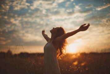 Woman in white dress embraces nature, bathed in sunset glow with arms wide open in field under a partially cloudy evening sky