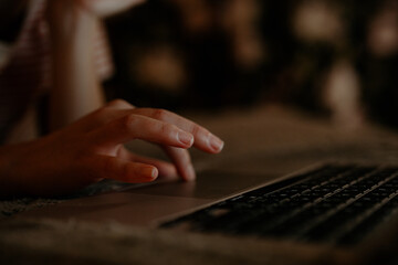A person is using a laptop late at night, illuminated by soft light. The focus is on their hand interacting with the keyboard while the surroundings create a warm atmosphere.