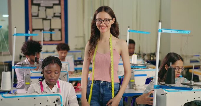 Indian young adult gen z happy female lady wear glass tape around neck cross arm indoor class room learn sewing craft course skill. Teen age pupil girl look cam fold hand do casual pose new day place