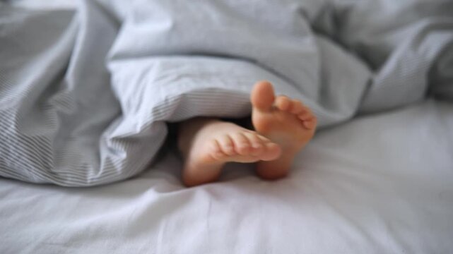 Little child's feet in bed covered with blanket