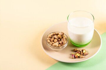 Pistachios in bowl beside glass of nut istachios milk on plate on pastel background with copy space