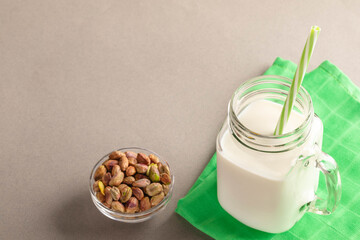 Pistachios in a bowl beside glass of milk with straw on green napkin Copy space for text