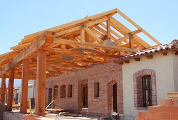 Unfinished, brick building showing exposed wooden framework under a clear, blue sky during daylight