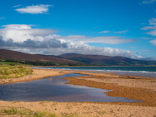 Clyne Burn Beach at Brora, in the Highlands of Northern Scotland, where the Clyne Burn River flows across the sands into the North Sea. Bright blue cloudy sky.