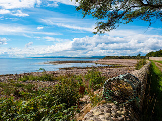 Dramatic clouds in a bright blue sky over the rocks, pebbles and shingles of a deserted beach at Golspie Cove on the east coast of the Scottish Highlands.