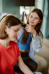 A young girl styles her sister's hair while sitting in a comfortable indoor space. The atmosphere is relaxed, emphasizing bonding and creativity between siblings.
