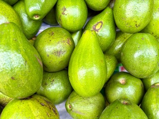 close-up, overhead shot of a large pile of fresh green avocados, some with natural spots, filling the entire frame.