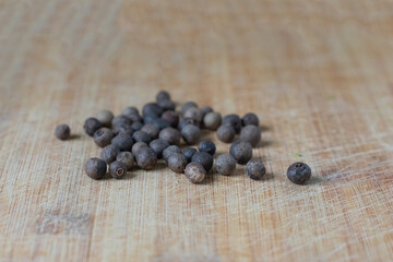 A pile of black peppercorns on a wooden cutting board