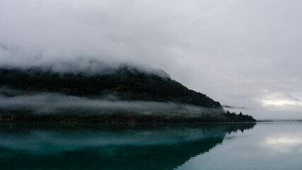 Quiet waters of Bergheimsvatnet mirror the misty landscape, revealing the enchanting beauty of Norways nature. A peaceful atmosphere captivates with soft clouds and tranquil vibes.