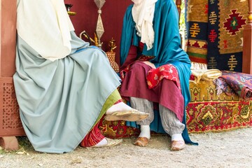 Two women in traditional middle eastern clothing sitting on cushions outdoors during a cultural...