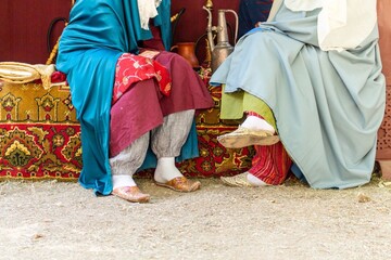 A group of women in traditional middle eastern clothing sitting on colorful carpets outdoors during a cultural event