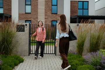 Two girls greet each other outside a contemporary residential property. One girl, dressed casually, approaches through a gated entrance while the other stands nearby. © m-art