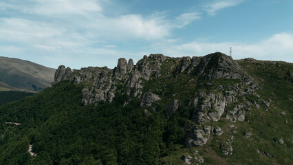 Rocky peaks of Babin Zub mountain in Stara Planina National Park, Serbia, rise above green forests under a blue sky. Aerial view from drone