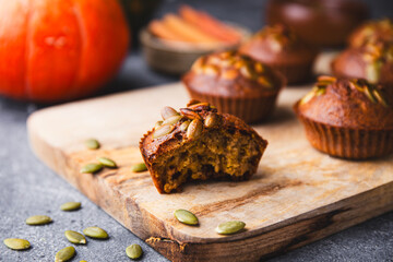 Autumn pumpkin cupcakes or baked muffins with fresh pumpkin and pumpkin seeds for Thanksgiving day on wooden cutting board close up