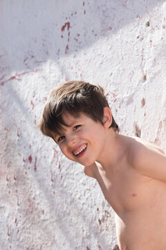 Ni&ntilde;o hispano sonriendo con el torso desnudo en un mediodia caluroso parado junto a un muro blanco