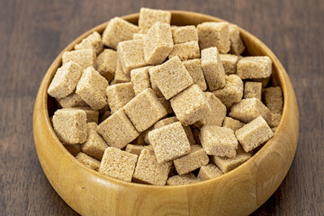 Organic brown sugar cubes in wooden bowl rustic style natural sweetener healthy ingredient close up textured surface kitchen table cozy atmosphere