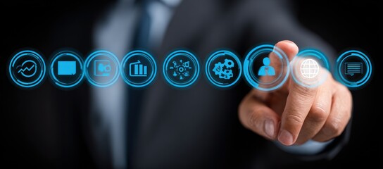 A person in a suit points at glowing, blue interface icons. The background is dark, highlighting the illuminated buttons. Digital concept is strong
