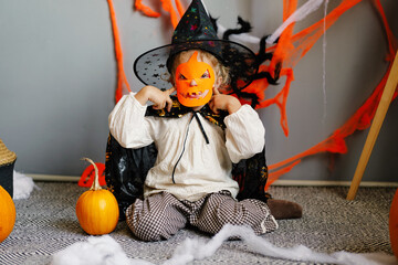 A joyful child sits among pumpkins and Halloween decor, wearing a charming costume and a carved pumpkin mask while celebrating the holiday