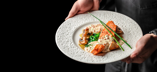 Chef holding a plate of grilled salmon with creamy sauce, spinach, and mushrooms on a white plate. copy space, top view