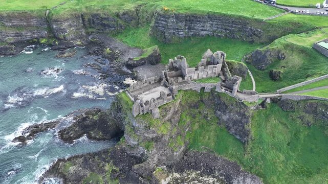 Luftaufnahme der historischen Ruinen von Dunluce Castle auf einer schroffen Klippe mit Blick auf die tosenden Wellen des Atlantischen Ozeans in Nordirland