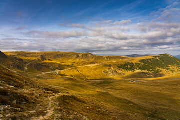 A solo traveler experiences a breathtaking autumn day in the wild Carpathian Mountains, near Lake Galcescu, in the Parang Mountains of Romania, where vibrant fall colors meet rugged peaks