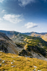A solo traveler experiences a breathtaking autumn day in the wild Carpathian Mountains, near Lake Galcescu, in the Parang Mountains of Romania, where vibrant fall colors meet rugged peaks
