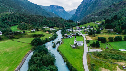 Enjoy the stunning vistas of Fortun, Norway, where vibrant green valleys meet clear blue waters. The quaint village rests alongside a meandering river, surrounded by majestic mountains.