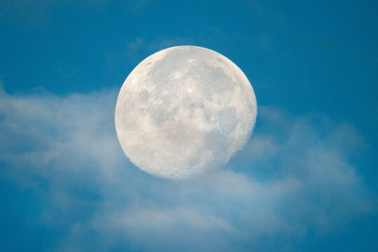 Detailed close-up of a full moon at dawn, slightly obscured by clouds